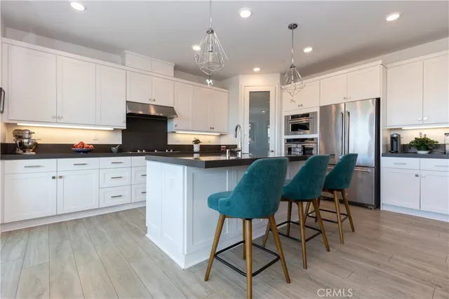 a kitchen with stainless steel appliances kitchen island granite countertop a refrigerator a stove a sink dishwasher and white cabinets with wooden floor