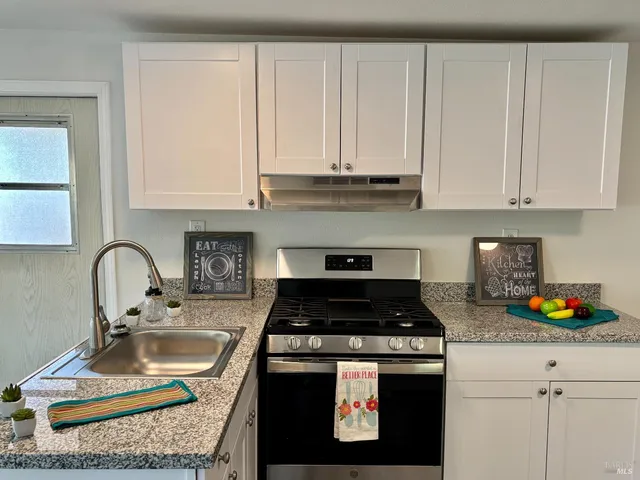 a kitchen with granite countertop a stove a sink and a white cabinets