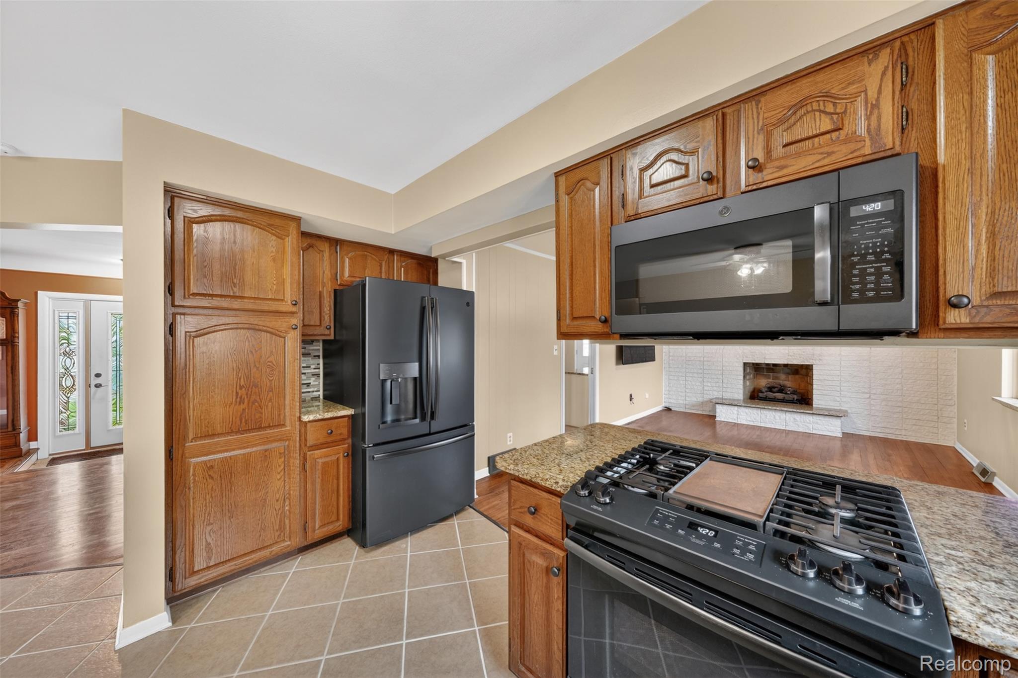 12014 Common Road Warren, MI 48093 - Photo 12 of 30 Kitchen with black stainless appliances, light tile patterned flooring, wood finish cabinetry, light stone counters, and decorative backsplash.