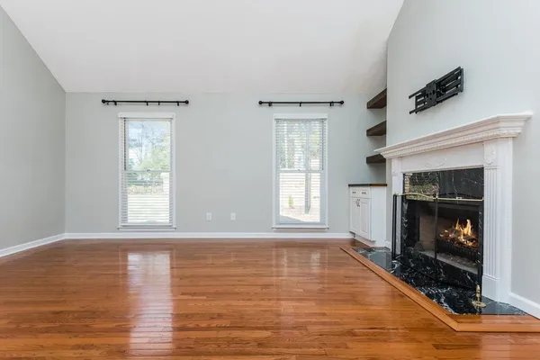 a view of an empty room with wooden floor fireplace and a window