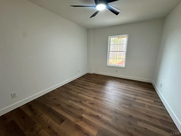 a view of an empty room and a ceiling fan wooden floor