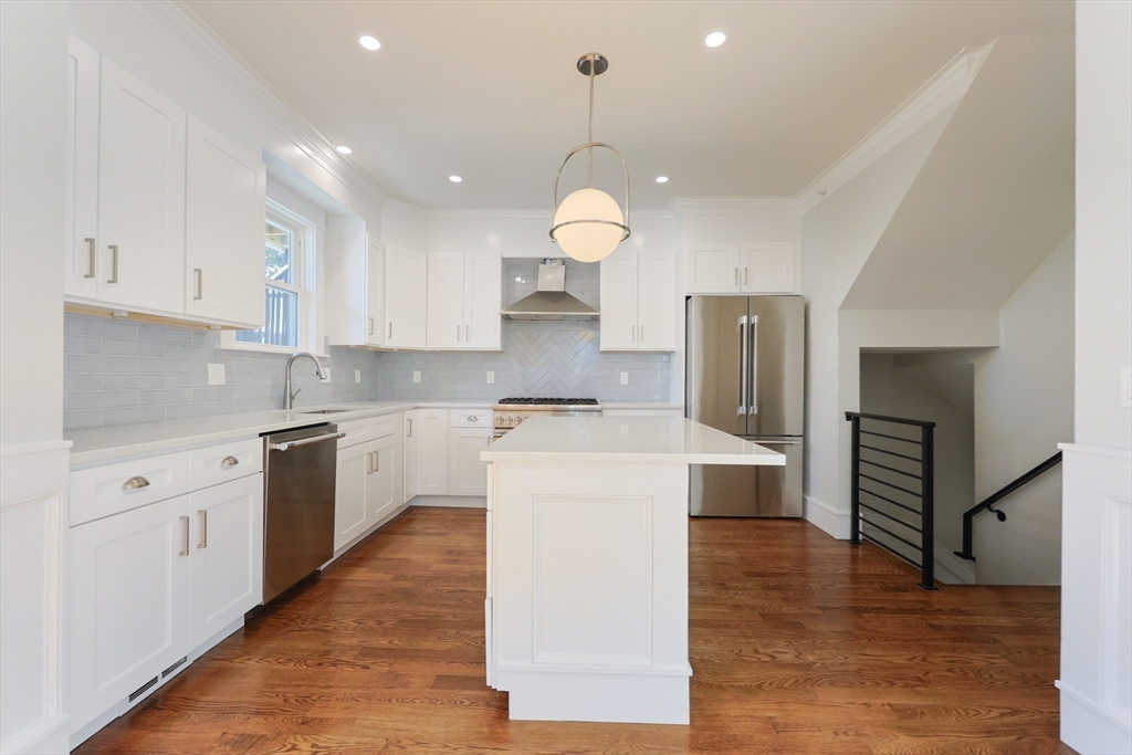 19 Fenwick Street, Unit 4 Somerville, MA 02145 - Photo 13 of 33 a large kitchen with kitchen island a stove a sink a refrigerator and white cabinets with wooden floor