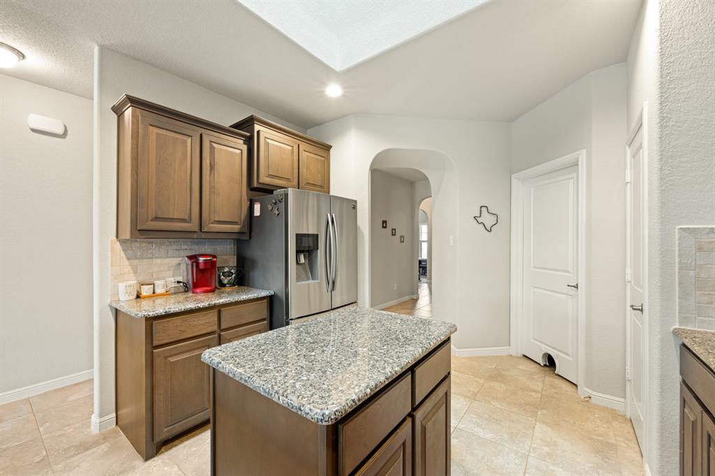 916 Falcon Road Argyle, TX 76226 - Photo 15 of 37 Kitchen featuring stainless steel refrigerator with ice dispenser, tasteful backsplash, a center island, light tile patterned floors, and light stone countertops