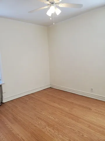 a view of an empty room with wooden floor and a ceiling fan