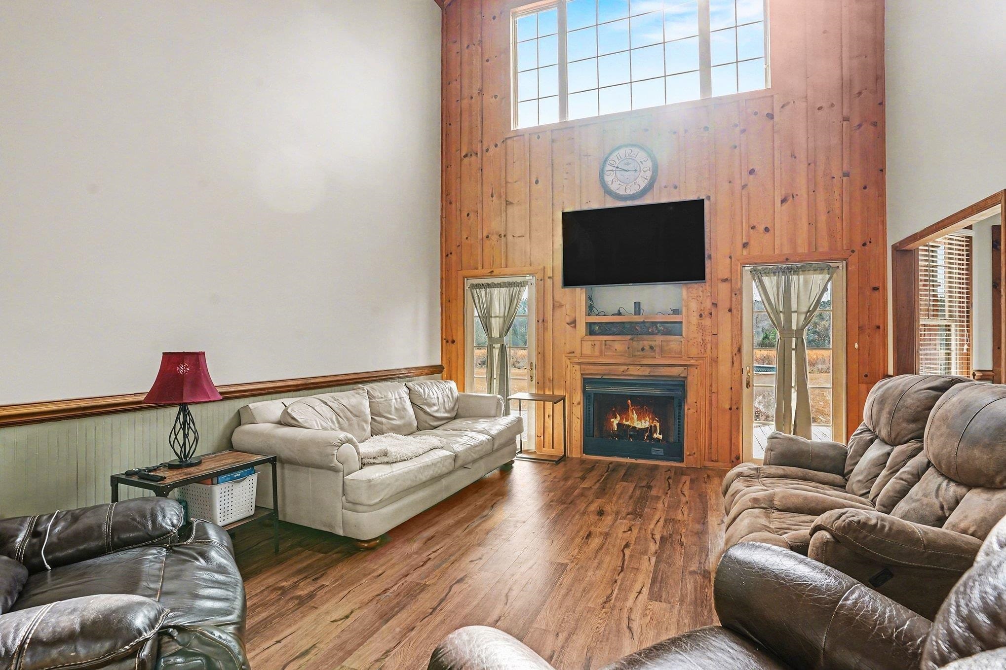 202 Highway 747 Loris Sc 29569 Loris, SC 29569 - Photo 4 of 34 Living room featuring wooden walls, a towering ceiling, wood finished floors, and a warm lit fireplace