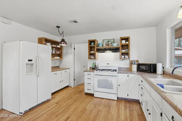 a kitchen with stainless steel appliances a stove top oven a sink a refrigerator and white cabinets with wooden floor