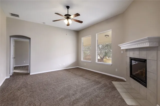 a view of an empty room with chandelier fan and fire place