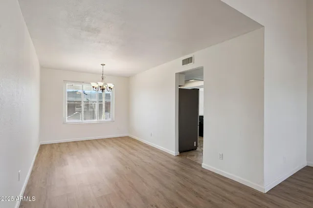 an empty room with wooden floor chandelier and windows