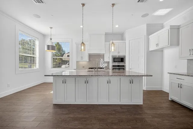 a kitchen with stainless steel appliances granite countertop a stove a sink dishwasher a refrigerator and white cabinets with wooden floor