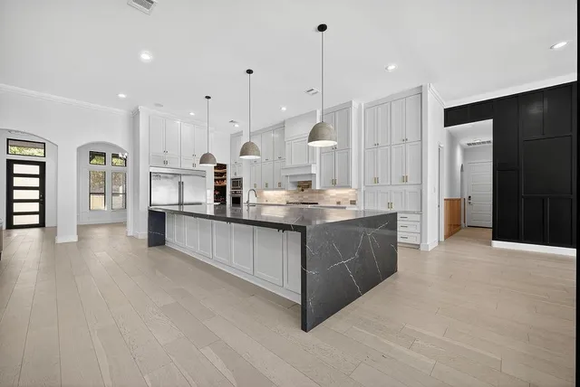 a large kitchen with stainless steel appliances kitchen island granite countertop a refrigerator a sink dishwasher and white cabinets with wooden floor