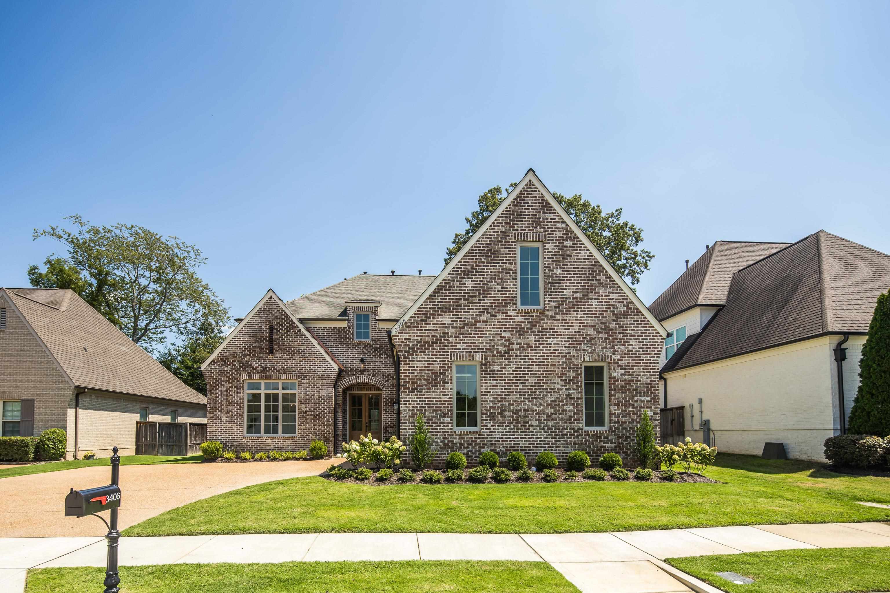 Brick exterior with gabled roof lines, landscaped front yard, paved driveway, and a concrete sidewalk
