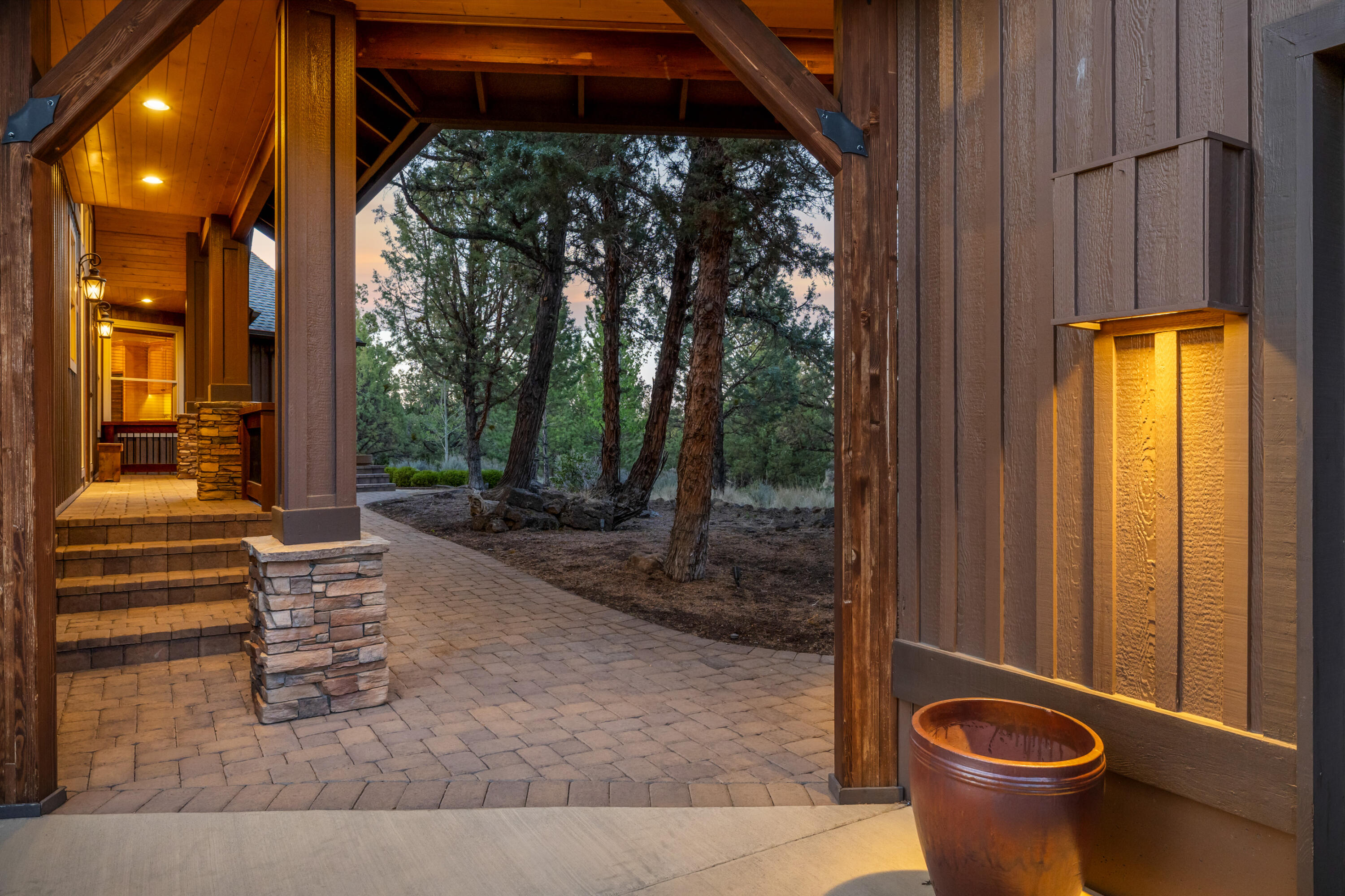 64145 Hunnell Road Bend, OR 97703 - Photo 5 of 65 A covered paver pathway leads to the home?s thoughtfully positioned entry, where the approach unfolds through mature trees and warm architectural details before opening inside to the landscaped grounds and Cascade Mountain views beyond.