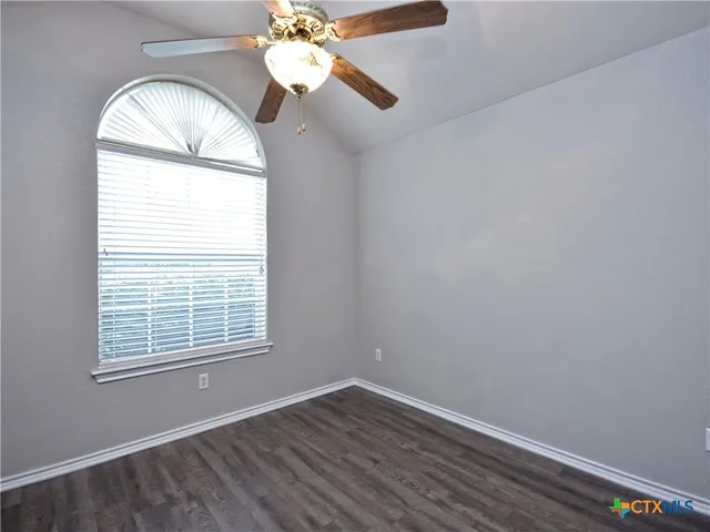 an empty room with wooden floor chandelier fan and windows