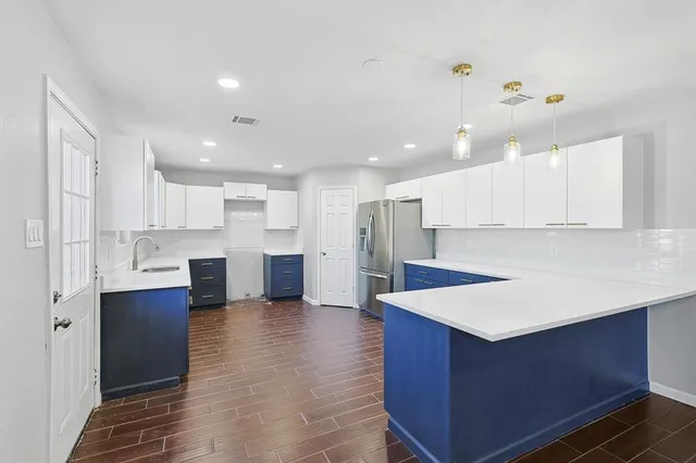 a large kitchen with kitchen island a sink dishwasher a refrigerator and white cabinets with wooden floor