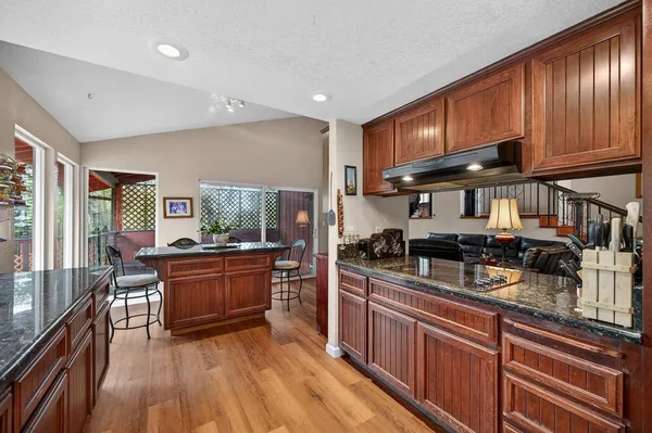 a kitchen with stainless steel appliances granite countertop wooden cabinets a sink dishwasher a stove and a refrigerator with wooden floor