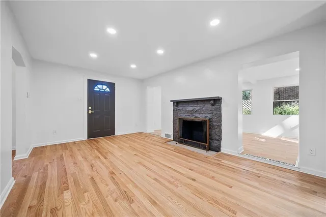 a view of an empty room with wooden floor fireplace and a window