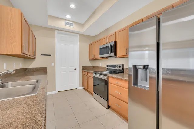 a kitchen with stainless steel appliances granite countertop a refrigerator a stove and a sink with wooden cabinets