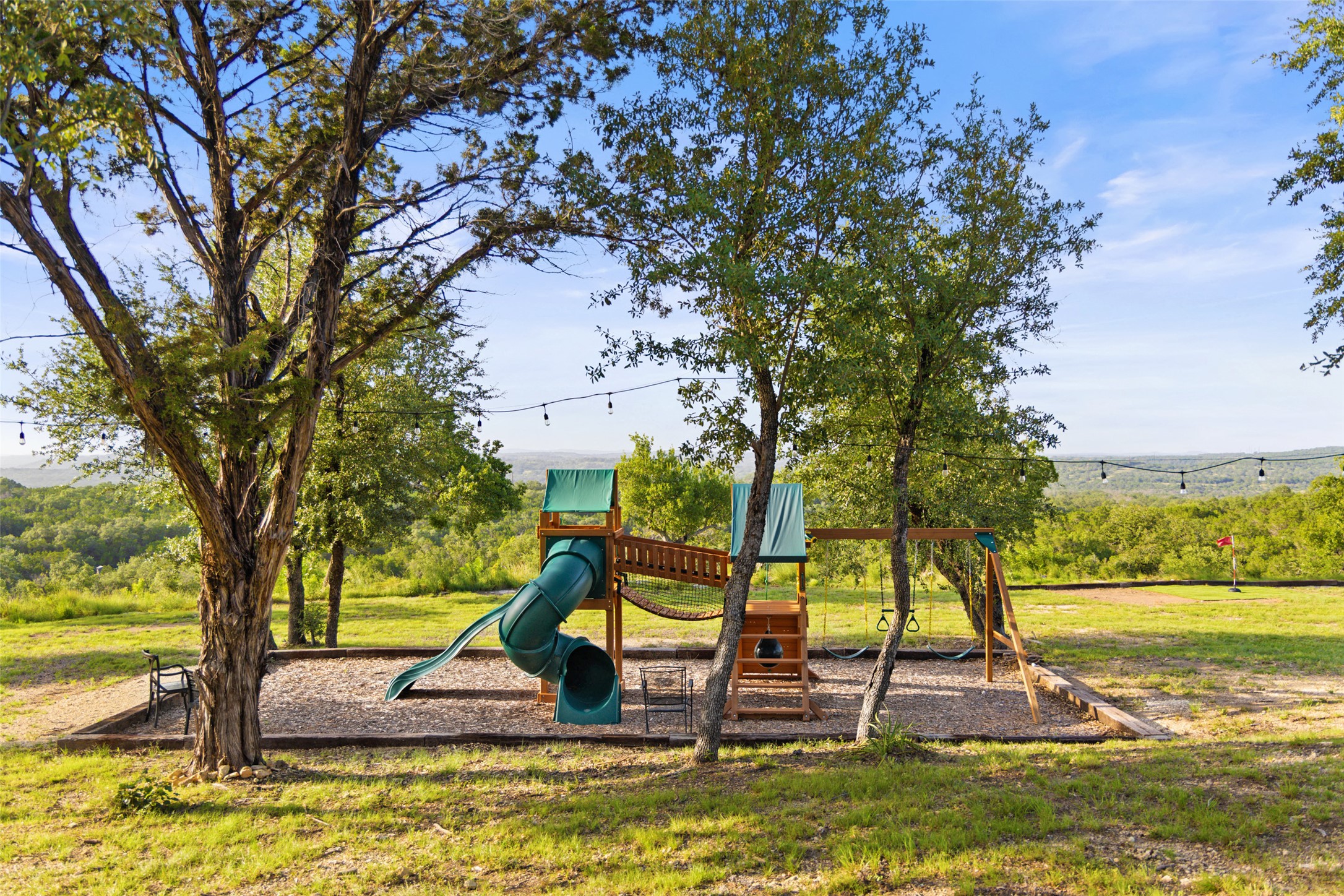 A spacious yard boasts a vibrant playground, perfect for endless outdoor recreation, set against a distant scenic backdrop.