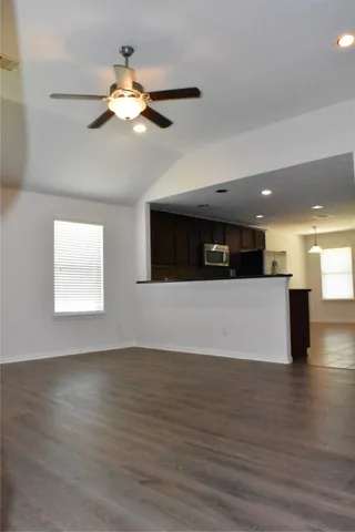 a view of an empty room with wooden floor and a ceiling fan