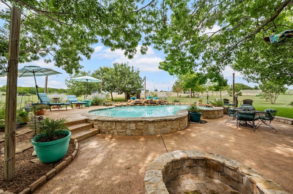 2141 Old Denton Road Decatur, TX 76234 - Photo 32 of 40 Outdoor living area featuring a gunite pool with a waterfall, a built-in fire pit, multiple seating areas on the patio, and mature trees providing natural shade