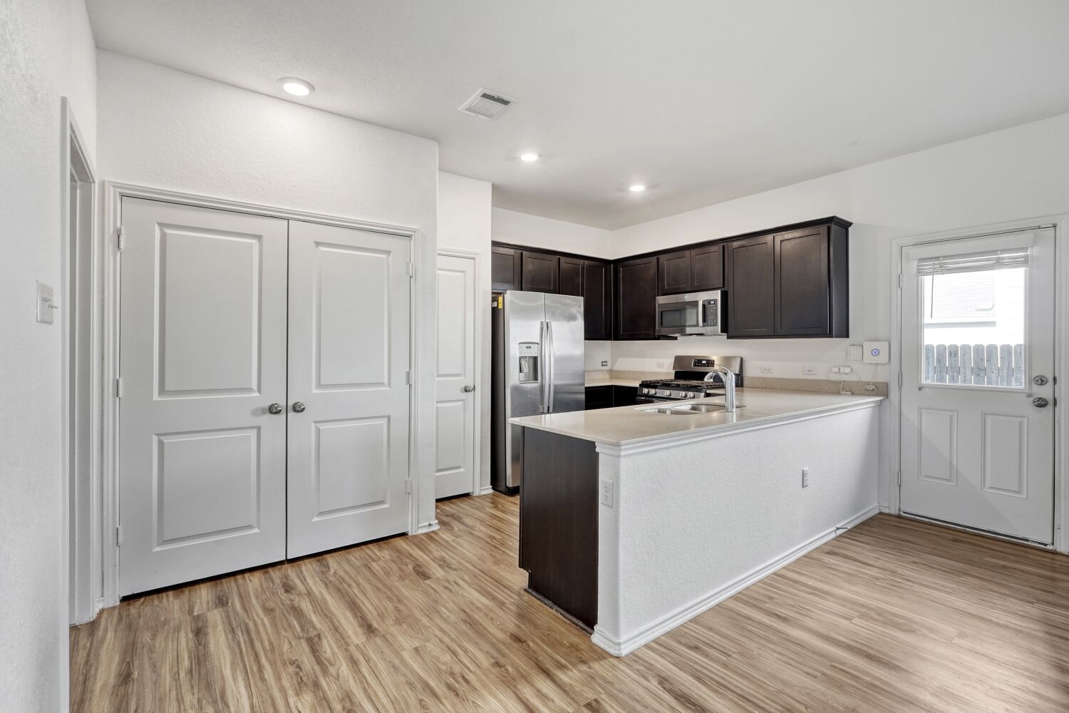 385 Geode Glen Maxwell, TX 78656 - Photo 7 of 16 Kitchen featuring stainless steel appliances, a peninsula, light wood-style floors, dark brown cabinets, and light stone countertops