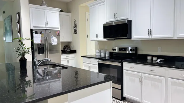 a kitchen with stainless steel appliances granite countertop a stove a sink a microwave a refrigerator and white cabinets