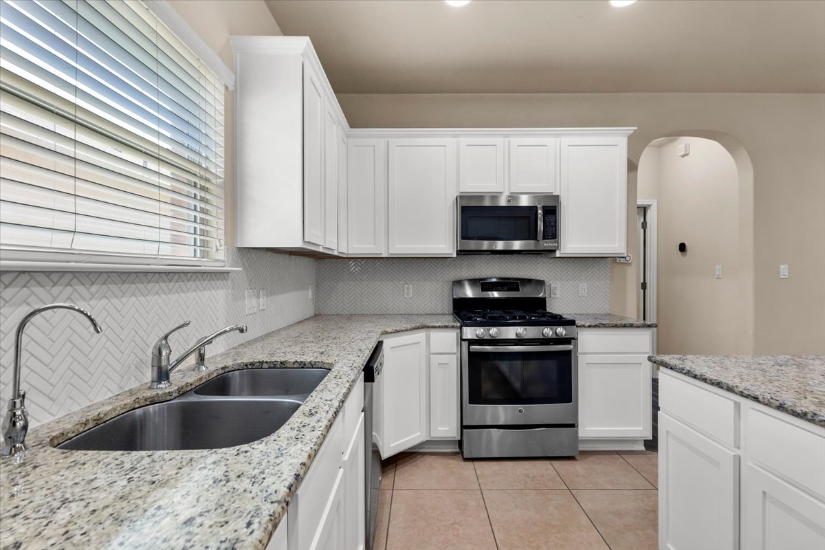 3451 Mayfield Ranch Boulevard, Unit 311 Round Rock, TX 78681 - Photo 11 of 40 Kitchen featuring white cabinetry, light-toned countertops, herringbone pattern backsplash, stainless steel appliances, and tile flooring