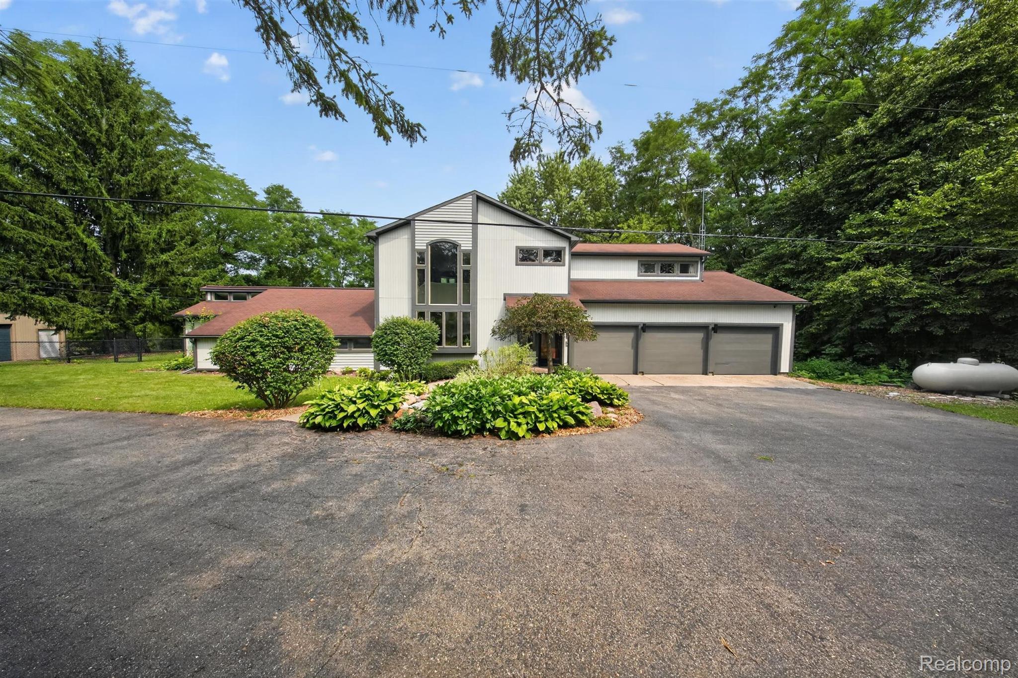 Contemporary architectural style featuring a multi-pane window facade, three-car garage, and mature landscaping