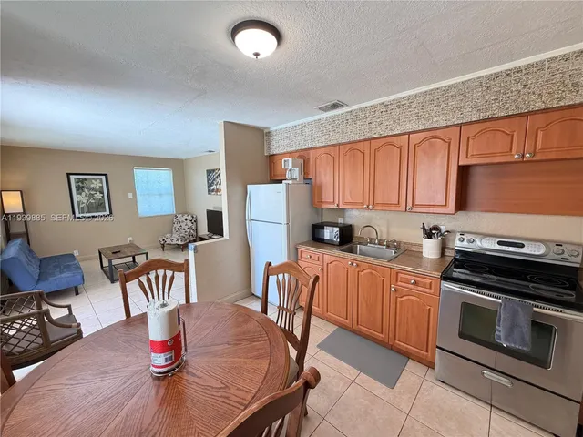 a kitchen with stainless steel appliances granite countertop a stove top oven a refrigerator a dining table and chairs with wooden floor