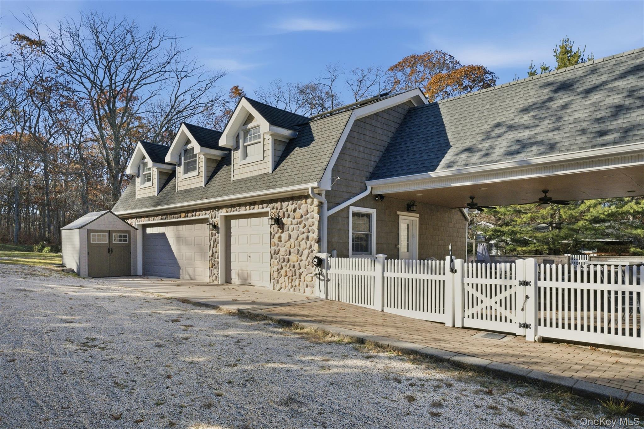 33 A Newtown Road Hampton Bays, NY 11946 - Photo 6 of 50 View of side of property featuring a gate, driveway, stone siding, a storage shed, and roof with shingles
