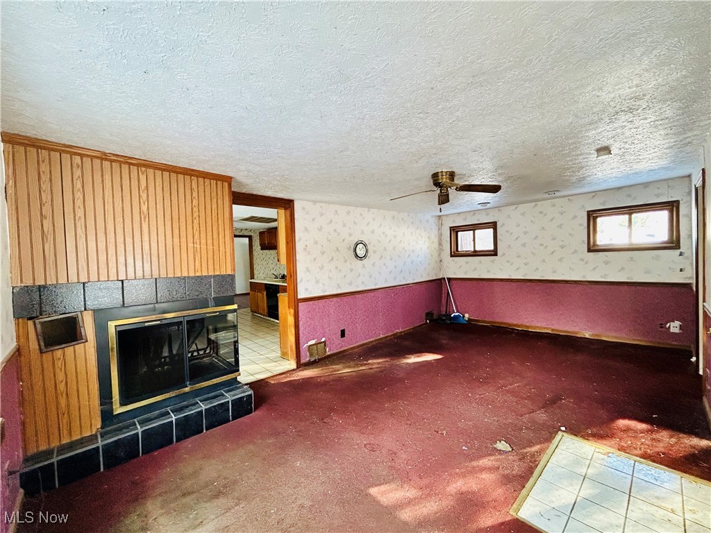 796 Rokeby Road Eastlake, OH 44095 - Photo 3 of 23 Unfurnished living room featuring wallpapered walls, carpet, a ceiling fan, a fireplace, and a textured ceiling