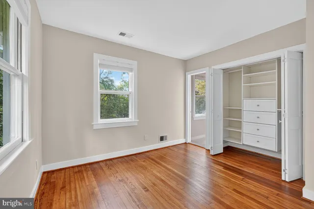 an empty room with wooden floor closet and windows