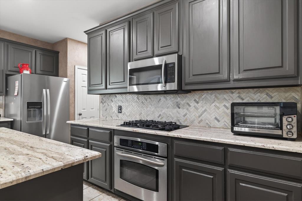 8708 Rugby Road Irving, TX 75063 - Photo 12 of 39 The kitchen features dark cabinetry, light granite countertops, a herringbone tile backsplash, and stainless steel appliances including a built-in oven, a gas cooktop, and an overhead microwave