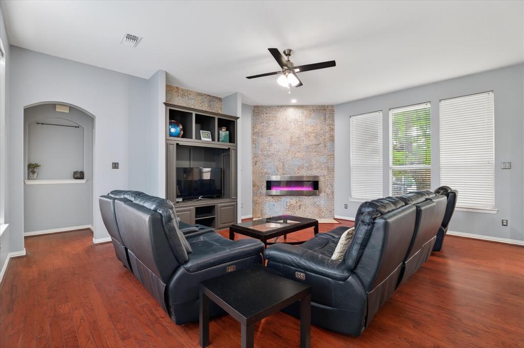 8708 Rugby Road Irving, TX 75063 - Photo 14 of 39 Living area featuring warm-toned hardwood floors, an accent wall with a modern linear fireplace, and three large windows providing natural light