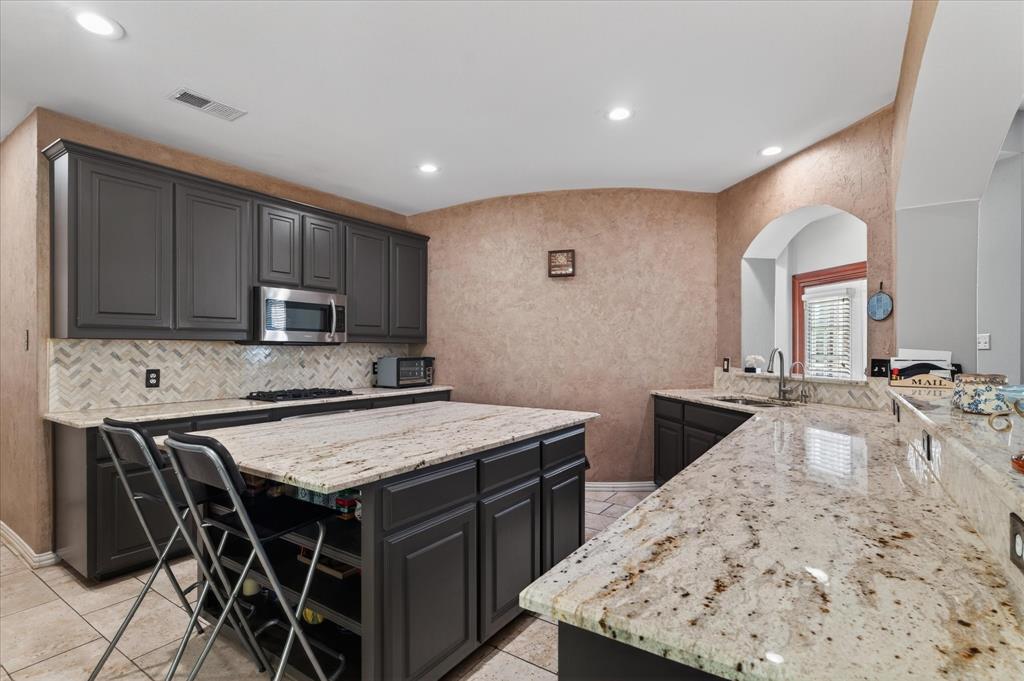 8708 Rugby Road Irving, TX 75063 - Photo 10 of 39 The kitchen features dark cabinetry, granite countertops, and a tile backsplash with a herringbone pattern