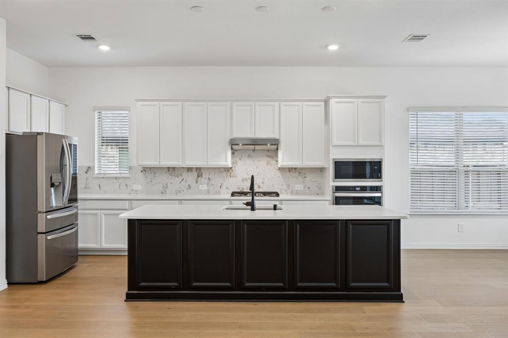 1303 Wheelwright Drive Forney, TX 75126 - Photo 16 of 39 Kitchen featuring a dark-toned island with a white countertop, stainless steel appliances, white cabinetry, a light-toned backsplash, and wood-finish flooring