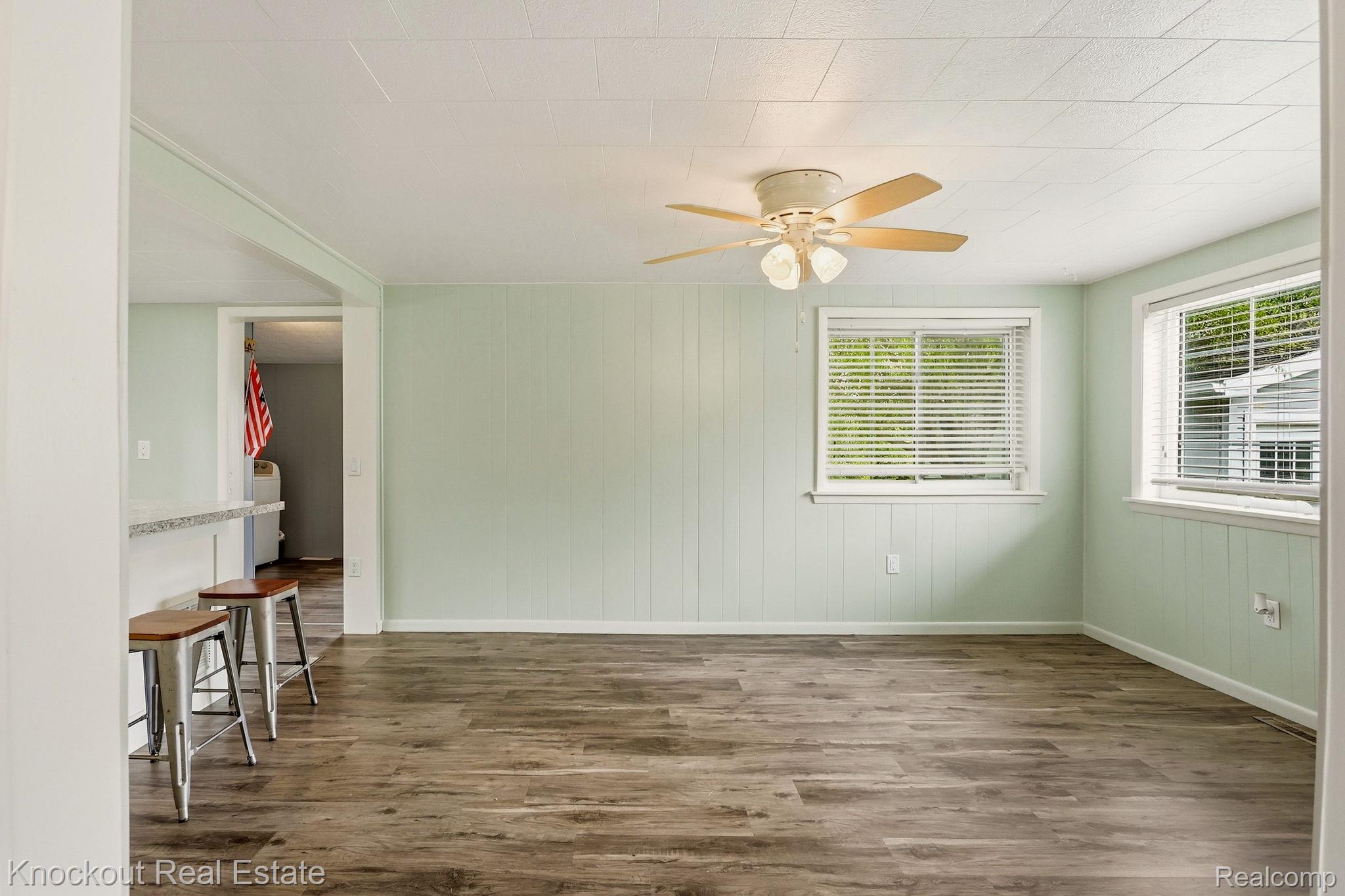 8771 Van Cleve Road Vassar, MI 48768 - Photo 12 of 44 Wood-finish flooring with light green paneled walls, ceiling fan with light kit, and multiple windows