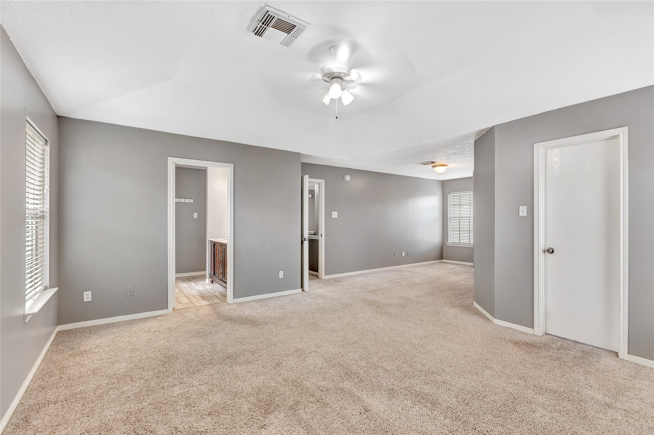 1007 Addison Park Lane Spring, TX 77373 - Photo 15 of 24 This spacious primary bedroom features soft carpet, soothing gray walls, ample natural light, and convenient access to its own bathroom, offering a perfect retreat for relaxation.