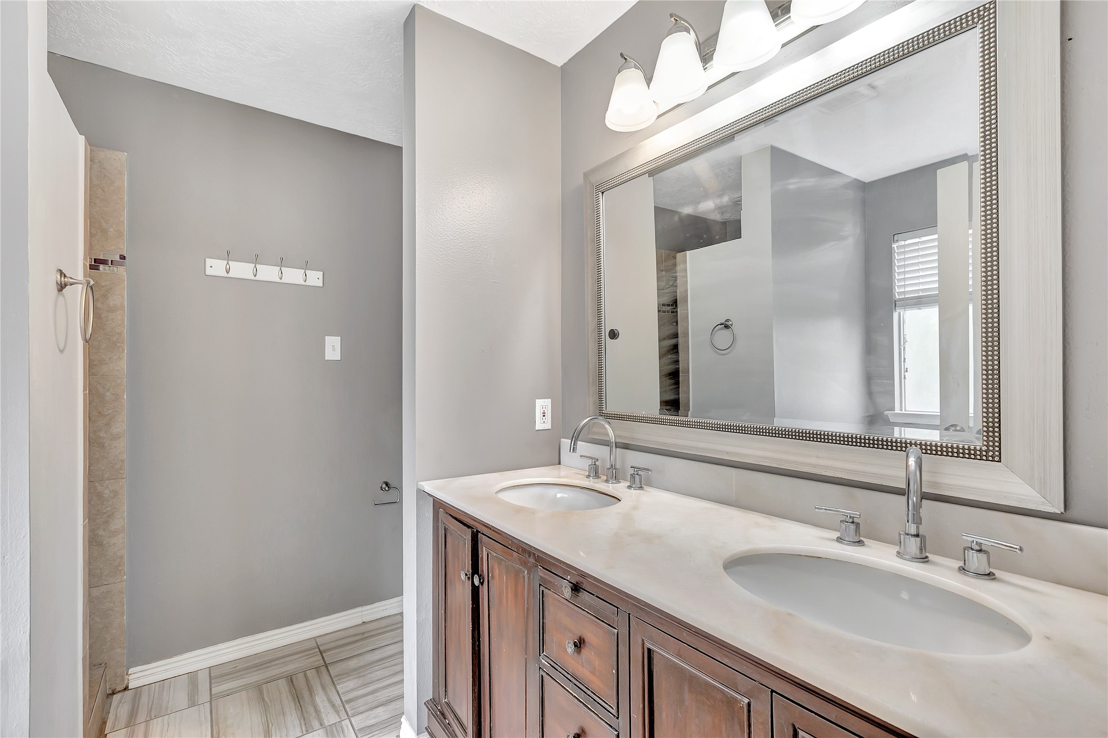 1007 Addison Park Lane Spring, TX 77373 - Photo 17 of 24 This elegant primary bathroom features a sophisticated double vanity with a large framed mirror, chic lighting, and a spacious walk-in shower, offering a perfect blend of style and functionality.