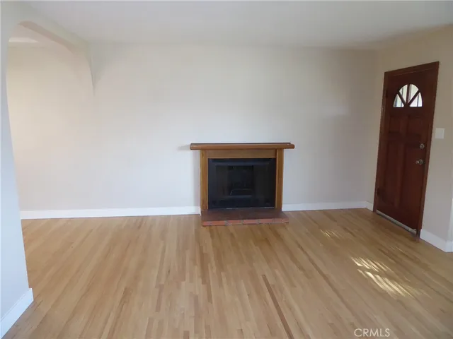 a view of an empty room with wooden floor and a fireplace