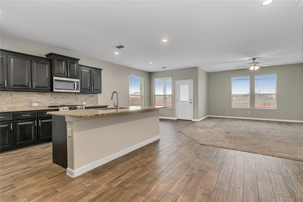 1102 Tiburon Trail Cleburne, TX 76033 - Photo 36 of 36 Kitchen with light stone counters, a kitchen island with sink, stainless steel microwave, open floor plan, and a ceiling fan