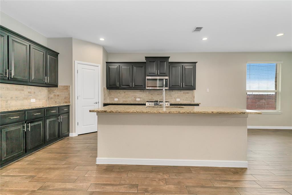 1102 Tiburon Trail Cleburne, TX 76033 - Photo 4 of 36 Kitchen featuring decorative backsplash, light wood-style floors, light stone countertops, stainless steel microwave, and an island with sink