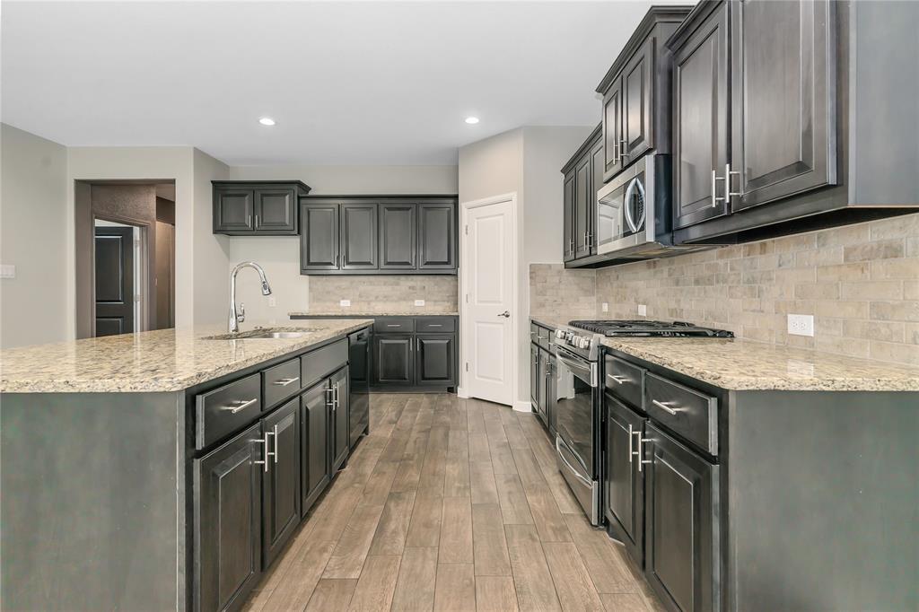 1102 Tiburon Trail Cleburne, TX 76033 - Photo 5 of 36 Kitchen featuring stainless steel appliances, light wood-style flooring, light stone countertops, an island with sink, and backsplash