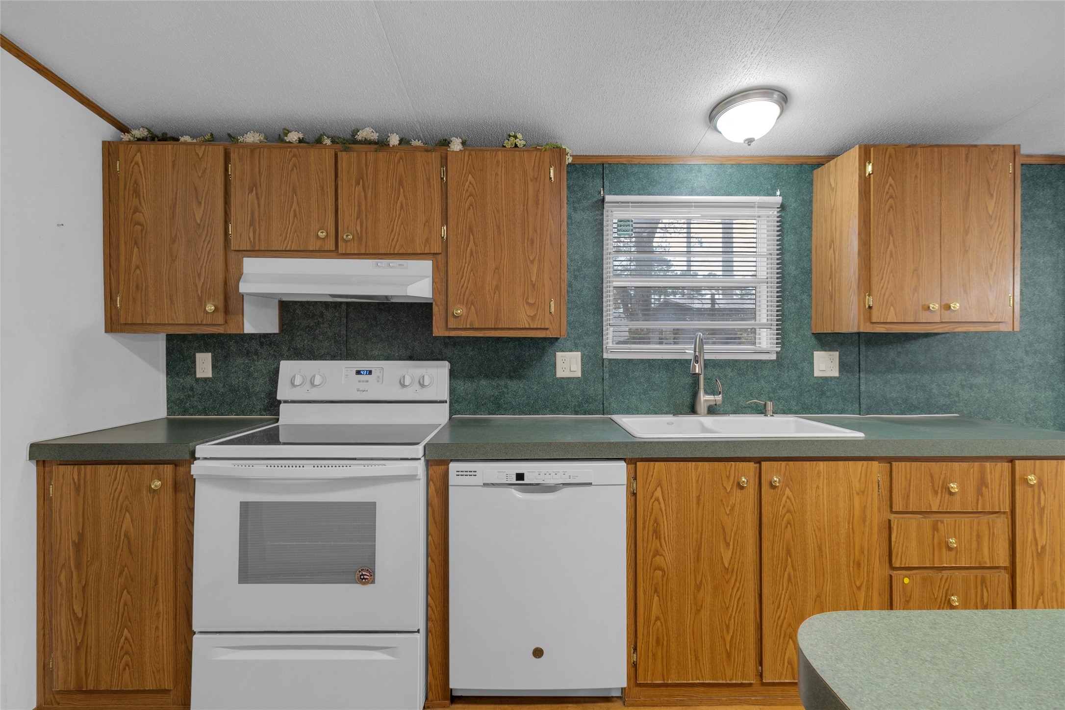 22094 Spear Road Porter, TX 77365 - Photo 7 of 45 This kitchen features wood cabinets, a white electric stove, and dishwasher, with a green countertop formica. It has a window above the sink for natural light and a ceiling light fixture.