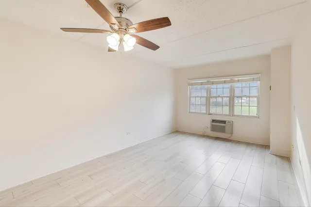 an empty room with wooden floor fan and windows