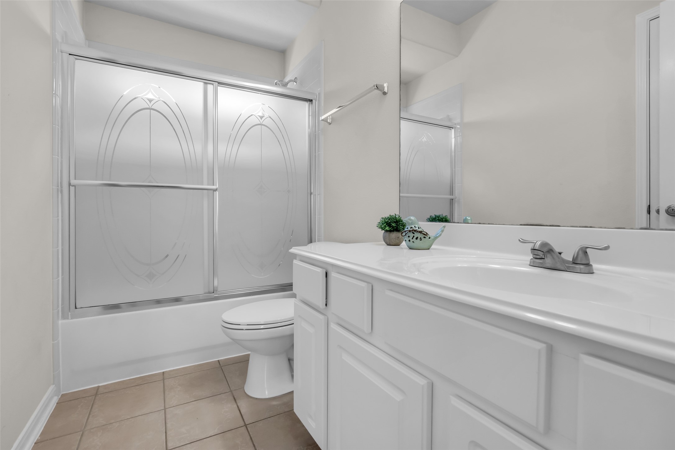 6807 Chapelfield Lane Houston, TX 77049 - Photo 31 of 42 This bathroom features a clean, modern design with a white vanity, a large mirror, and a frosted glass shower/tub enclosure. Neutral tile flooring adds a classic touch.