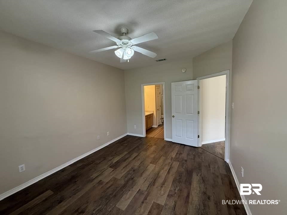 2651 South Juniper Street, Unit 401 Foley, AL 36535 - Photo 21 of 27 Unfurnished bedroom featuring connected bathroom, ceiling fan, visible vents, baseboards, and dark wood-style flooring