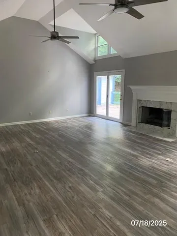 an empty room with wooden floor a ceiling fan a fireplace and windows