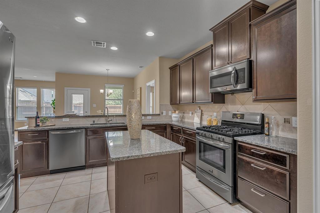 3812 Fordham Street Frisco, TX 75036 - Photo 13 of 33 Kitchen with appliances with stainless steel finishes, backsplash, dark brown cabinetry, light stone counters, and light tile patterned floors