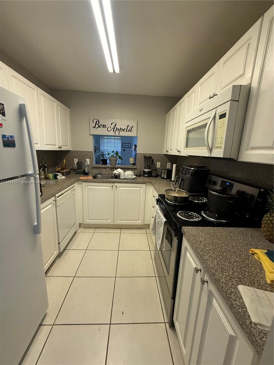 7145 Northwest 173rd Drive, Unit 1106 Hialeah, FL 33015 - Photo 13 of 17 a kitchen with a sink a stove top oven a refrigerator and cabinets